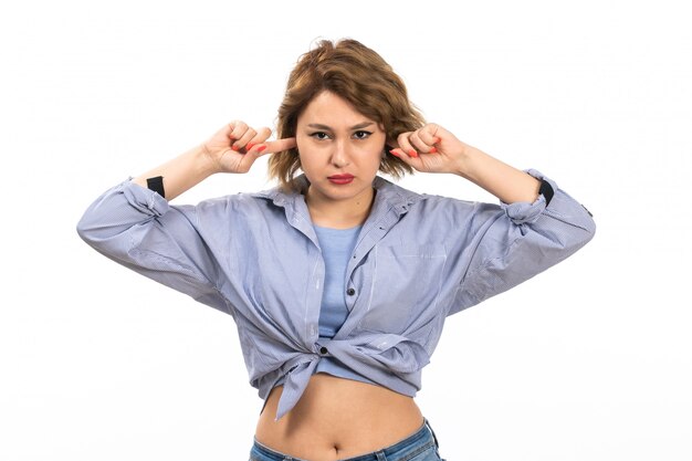 Una giovane bella ragazza di vista frontale in camicia blu e blue jeans che coprono le sue orecchie sul bianco