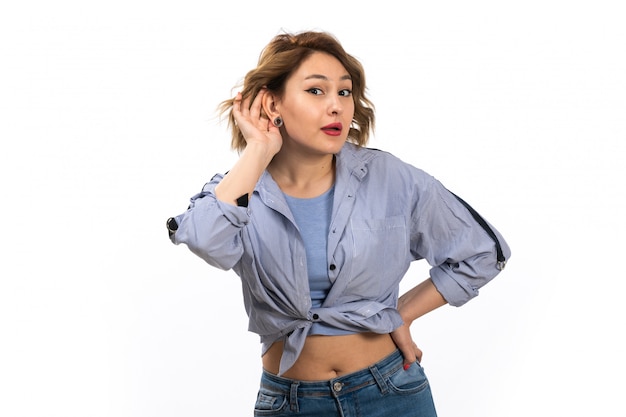 Una giovane bella ragazza di vista frontale in camicia blu e blue jeans che provano a sentire fuori in posa