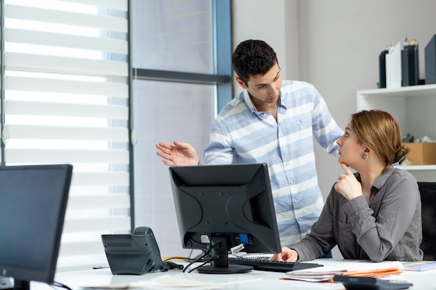 Una giovane bella signora di vista frontale in camicia grigia che parla e che discute qualcosa con il giovane dentro l'ufficio durante l'attività di lavoro della costruzione di giorno