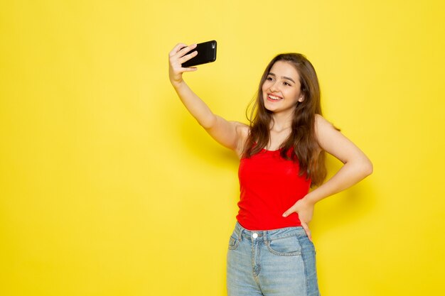 Una giovane bella signora di vista frontale in camicia rossa e blue jeans che prendono un selfie