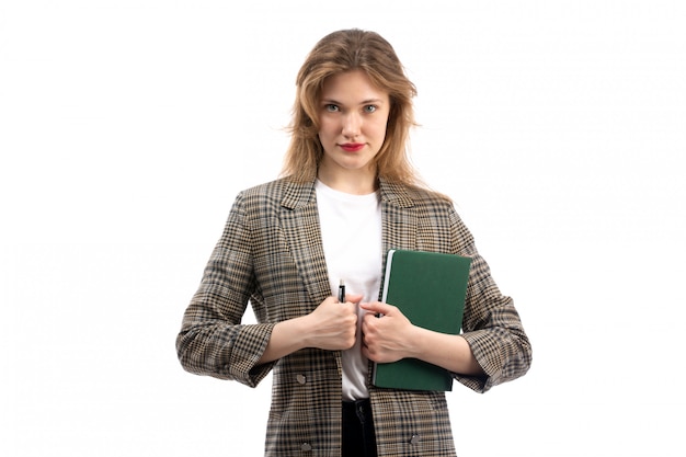 Una giovane bella signora di vista frontale in jeans e cappotto neri della maglietta bianca che tengono libro verde e penna sul bianco