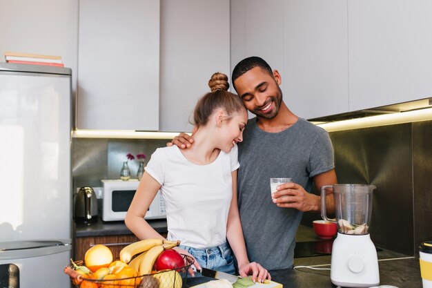 Una giovane coppia che fa colazione in cucina. Uomini e donne in maglietta che si abbracciano, cucinano insieme, la coppia si abbraccia con facce felici