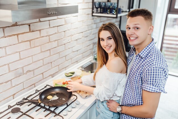 Una giovane coppia di sposi positiva, una ragazza affascinante e un bel ragazzo preparano la frittata in cucina..