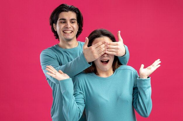 Una giovane coppia sorridente il giorno di San Valentino ha coperto gli occhi delle ragazze con le mani isolate su sfondo rosa