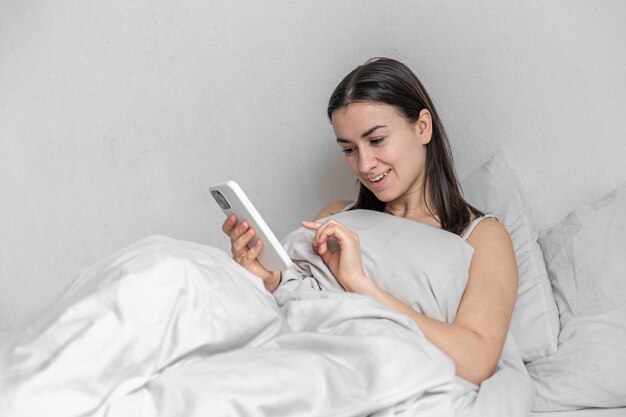 Una giovane donna a letto con lo smartphone al mattino