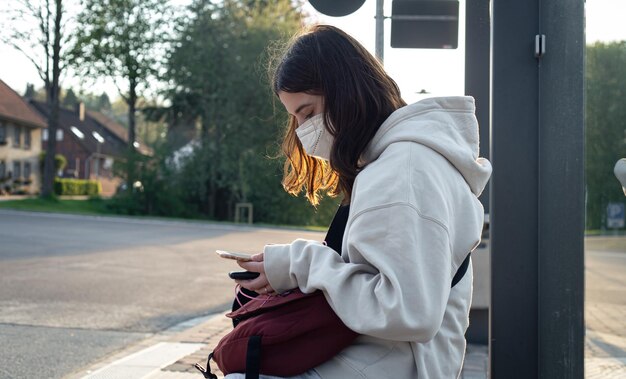 Una giovane donna adolescente sta aspettando un autobus alla fermata dell'autobus la mattina presto