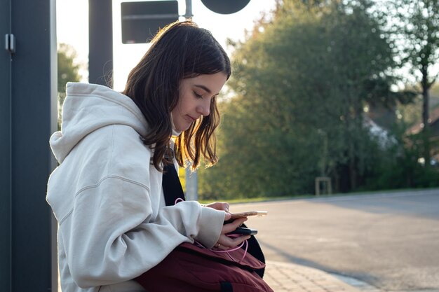 Una giovane donna adolescente sta aspettando un autobus alla fermata dell'autobus la mattina presto