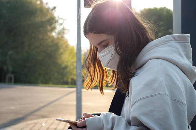 Una giovane donna adolescente sta aspettando un autobus alla fermata dell'autobus la mattina presto