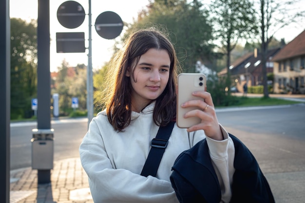 Una giovane donna adolescente sta aspettando un autobus alla fermata dell'autobus la mattina presto