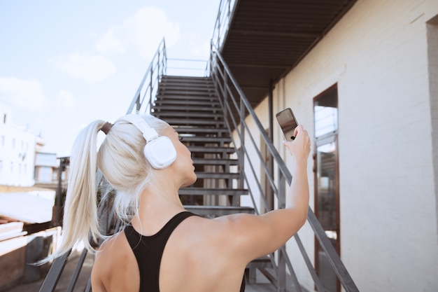 Una giovane donna atletica in camicia e cuffie bianche che risolvono ascoltando la musica su una scala all'aperto