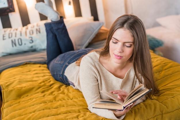 Una giovane donna attraente che gode leggendo il libro sul letto