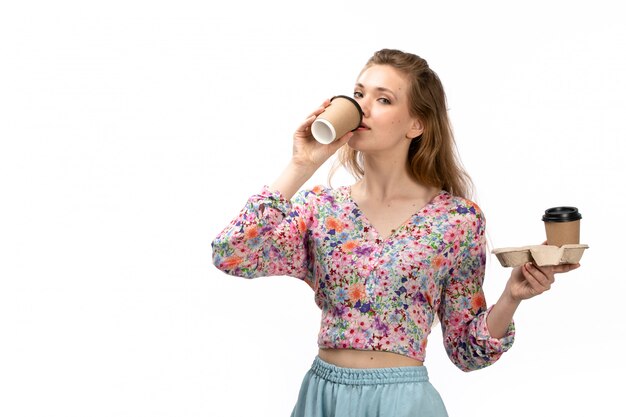 Una giovane donna attraente di vista frontale in camicia colorata e gonna blu, bere il caffè sul bianco