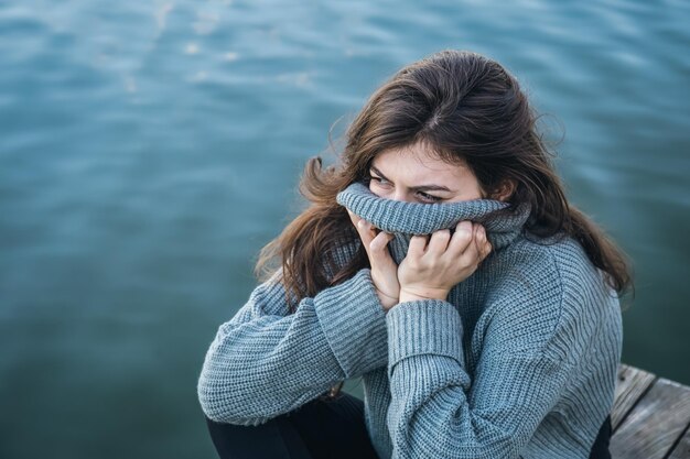 Una giovane donna attraente in un maglione si siede vicino al fiume