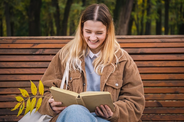 Una giovane donna attraente si siede su una panchina in un parco autunnale e legge un libro