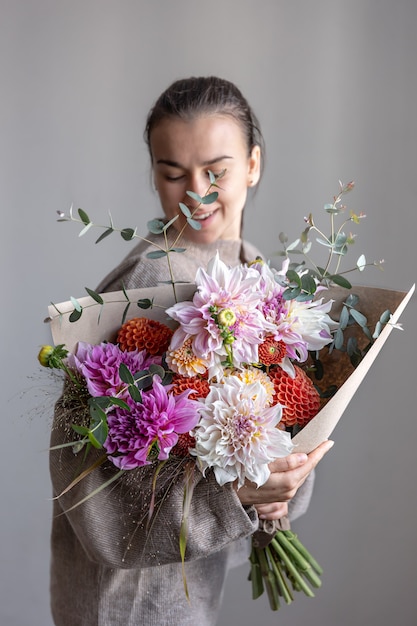 Una giovane donna attraente sorride e tiene in mano un grande bouquet festivo con crisantemi e altri fiori.