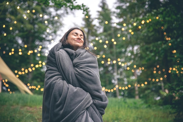 Una giovane donna avvolta in una coperta nella foresta su uno sfondo sfocato