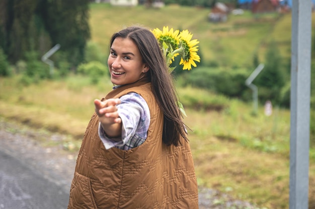 Una giovane donna cammina in montagna con un mazzo di girasoli