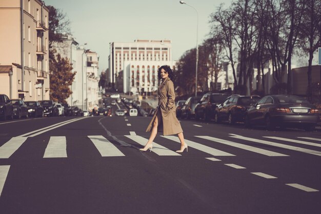 una giovane donna cammina per la città autunnale, una femmina dal corpo felice con i capelli ricci in un impermeabile.