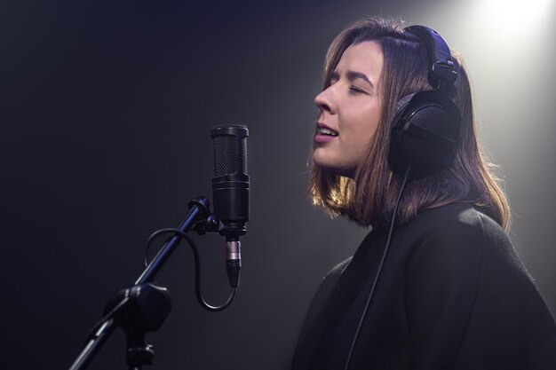 Una giovane donna carina con le cuffie canta in un microfono in una stanza buia