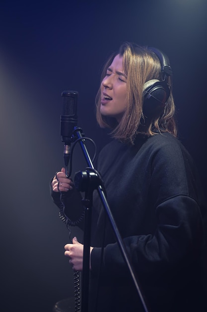 Una giovane donna carina con le cuffie canta in un microfono in una stanza buia