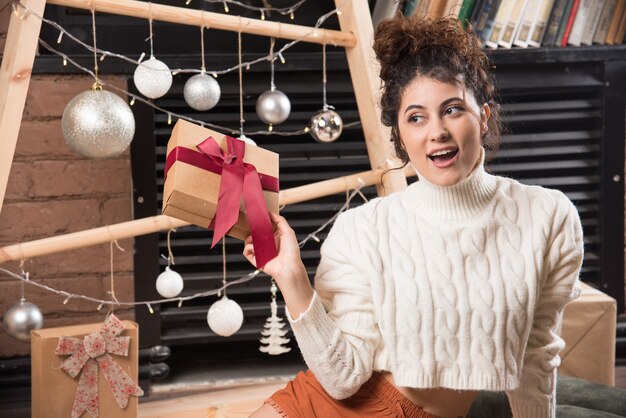 Una giovane donna che guarda lontano e tiene in mano una confezione regalo con un fiocco