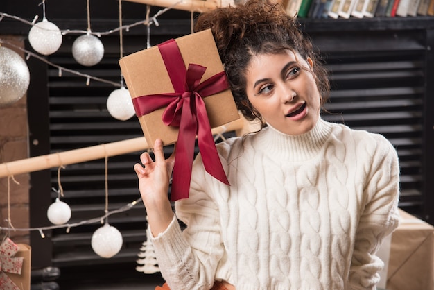 Una giovane donna che guarda lontano e tiene in mano una confezione regalo con un fiocco