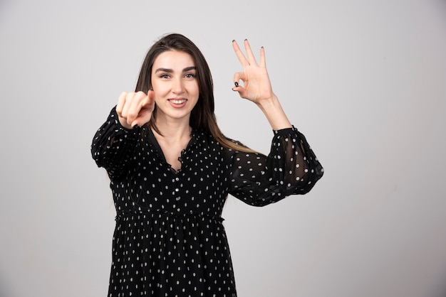 Una giovane donna che punta alla telecamera su un muro grigio. Foto di alta qualità