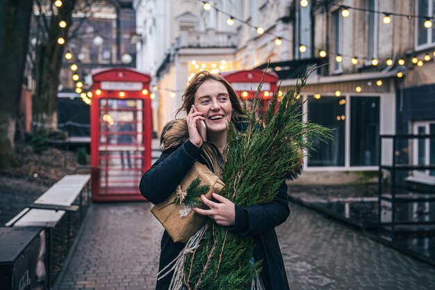 Una giovane donna con un albero di Natale e una confezione regalo che parla al telefono