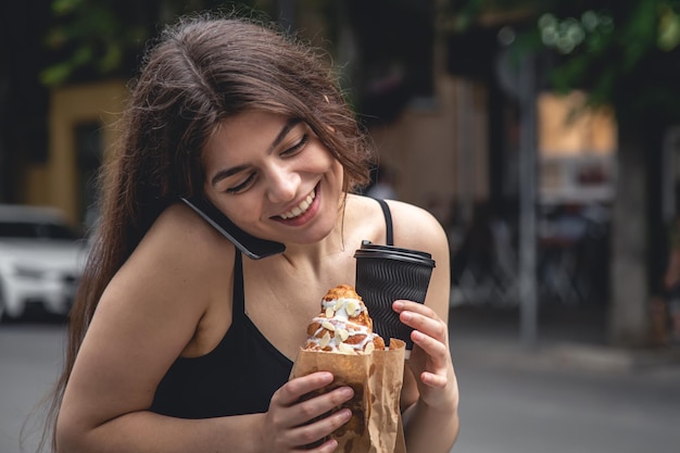 Una giovane donna con un croissant e una tazza di caffè durante una passeggiata in città.