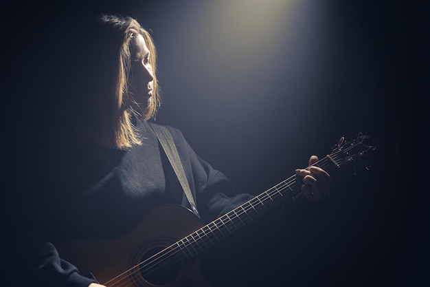 Una giovane donna con una chitarra acustica nel buio sotto un raggio di luce