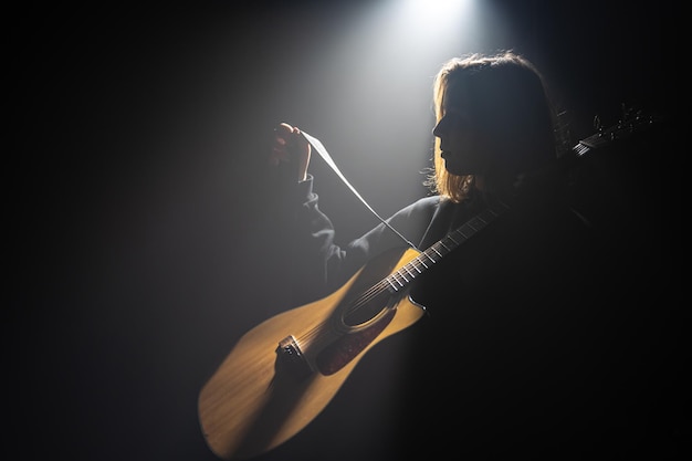 Una giovane donna con una chitarra acustica nel buio sotto un raggio di luce
