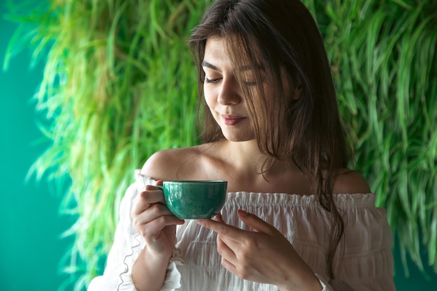 Una giovane donna con una tazza di caffè sullo sfondo con piante verdi