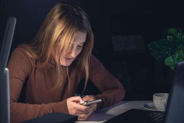 Una giovane donna con uno smartphone in mano lavora a tarda notte