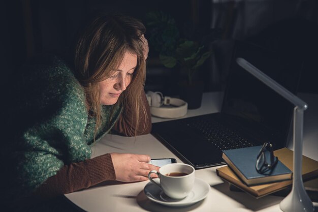 Una giovane donna con uno smartphone in mano lavora a tarda notte