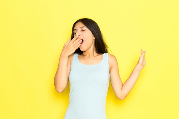 Una giovane donna di vista frontale in camicia blu in posa e starnuti sullo sfondo giallo ragazza posa modello