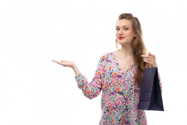Una giovane donna di vista frontale in camicia disegnata fiore e pantaloni neri che tengono sorridere dei pacchetti di acquisto