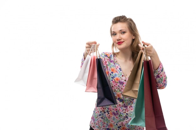 Una giovane donna di vista frontale in camicia disegnata fiore e pantaloni neri che tengono sorridere dei pacchetti di acquisto