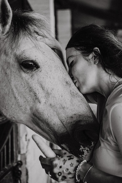 Una giovane donna e un cavallo, sentimenti, cure, affetto, tenerezza, una donna abbraccia e bacia un cavallo. Chiuda in su della giovane donna felice che abbraccia il suo cavallo.