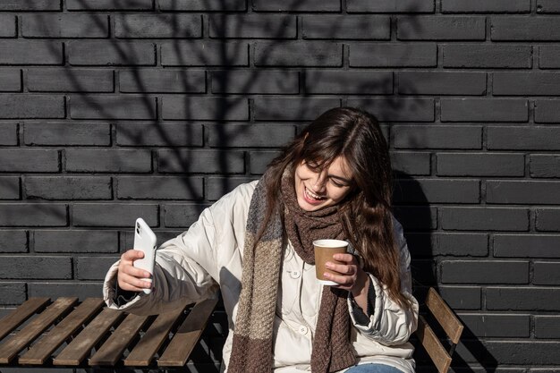 Una giovane donna fotografa un bicchiere di bevanda calda durante una passeggiata in città