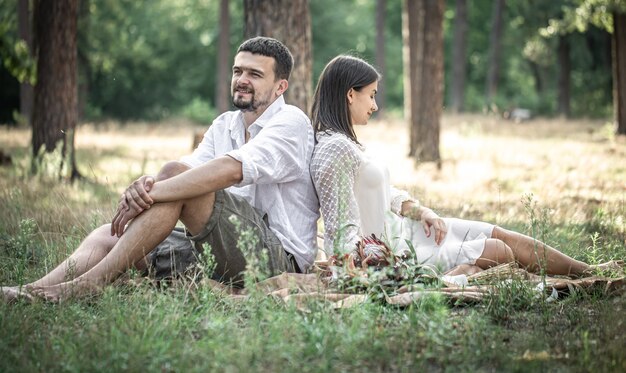 Una giovane donna in abito bianco e un uomo in camicia sono seduti nella foresta sull'erba, un appuntamento in natura, una storia d'amore nel matrimonio.