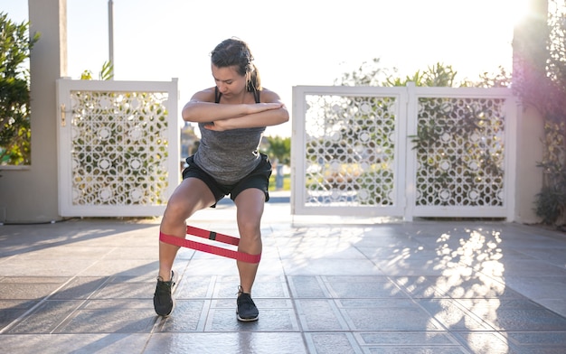 Una giovane donna in canottiera e pantaloncini fa sport con un espansore all'aria aperta.