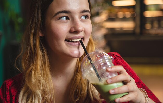 Una giovane donna in un caffè beve una bevanda verde latte ghiacciato