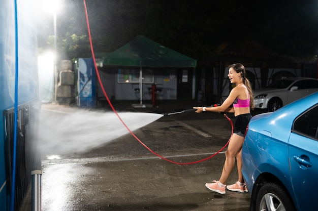 Una giovane donna lava un'auto blu in un autolavaggio