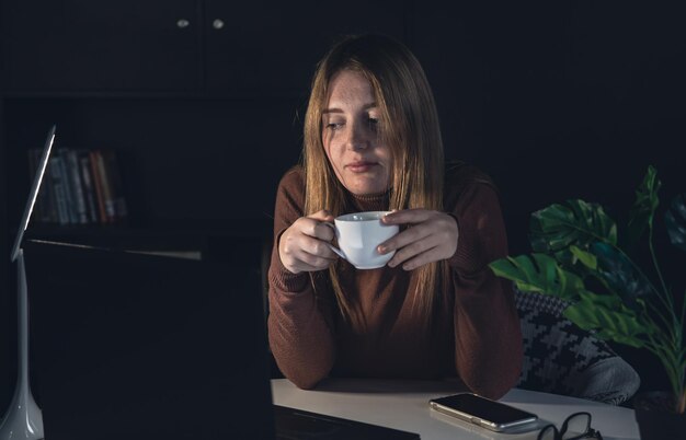 Una giovane donna lavora di notte dietro un laptop con una lampada accesa