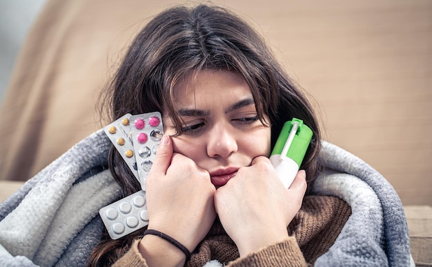 Una giovane donna malata che tiene in mano uno spray per la tosse e delle pillole