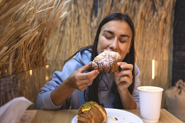 Una giovane donna mangia croissant con caffè in un bar