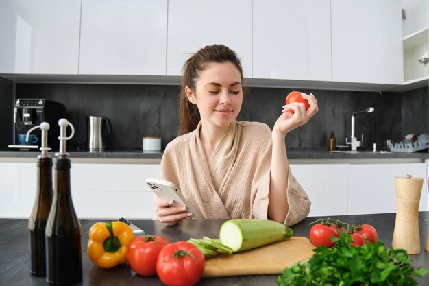 Una giovane donna ordina la spesa sull'app mobile. Una ragazza in accappatoio si siede in cucina con le verdure