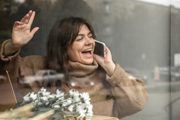 Una giovane donna parla al telefono e saluta qualcuno, vista dalla strada.