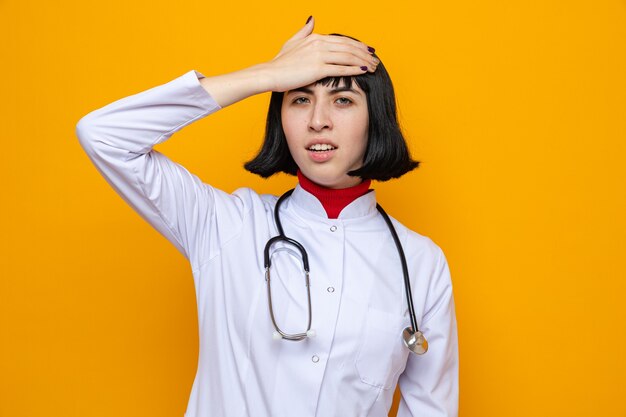 Una giovane donna piuttosto caucasica delusa in uniforme da medico con stetoscopio mette la mano sulla fronte