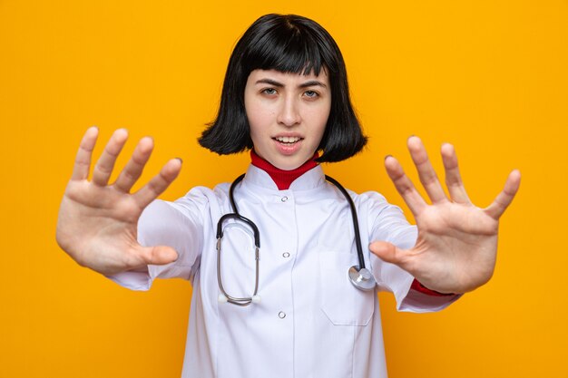 Una giovane donna piuttosto caucasica scontenta in uniforme da medico con uno stetoscopio che allunga le mani